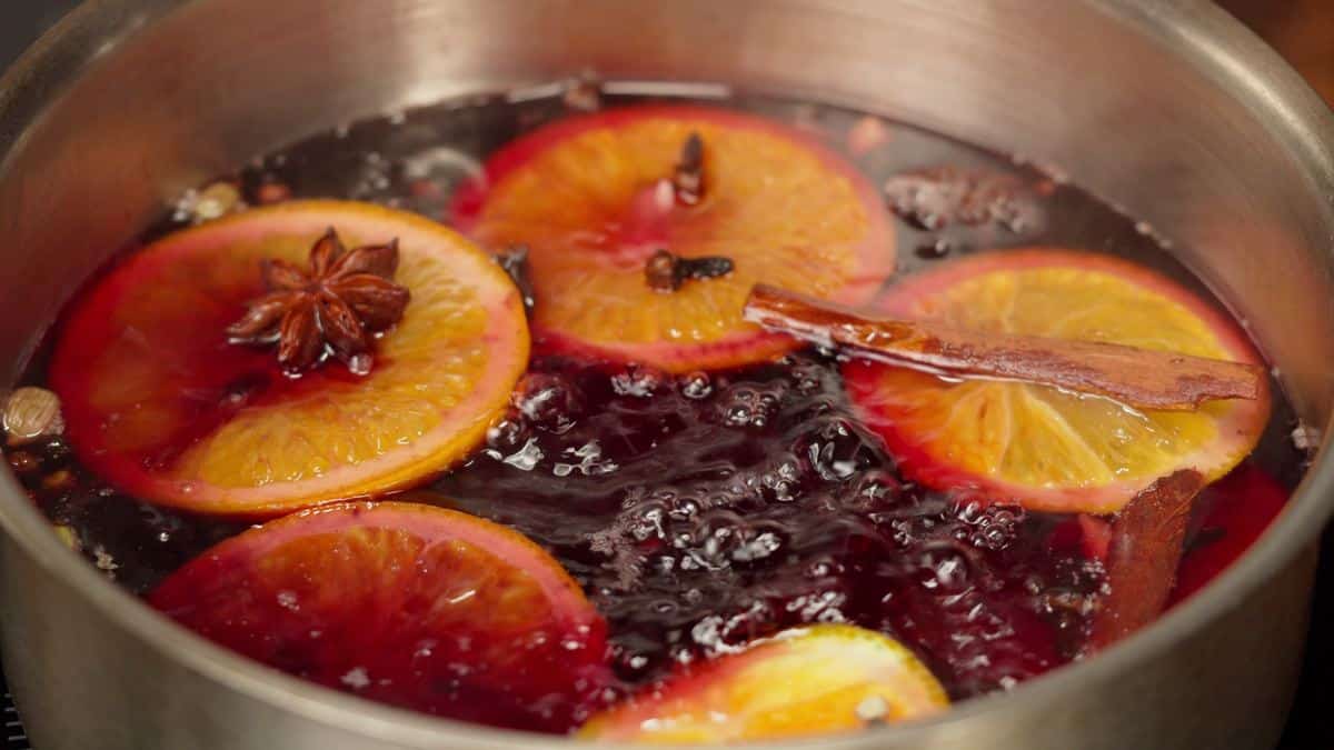 Citrus slices, cinnamon sticks, and star anise simmering in a pot on the stove
